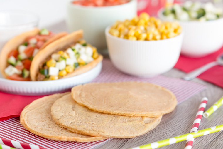 tacobröd i förgrunden med fyllda tacos bakom och skålar med tillbehör, av Anna Winér